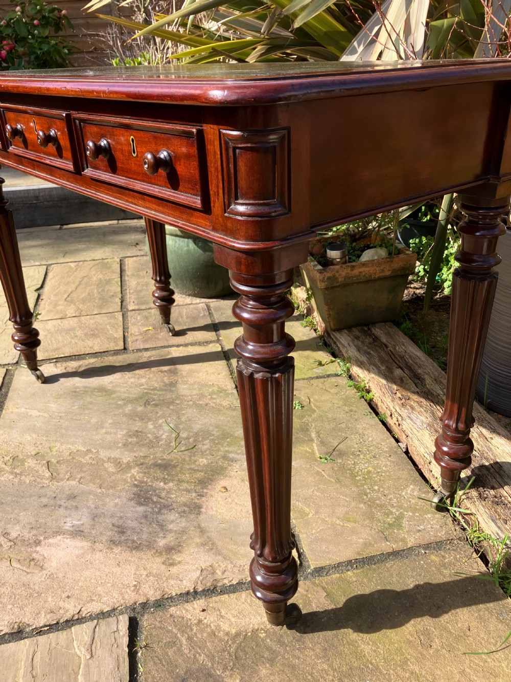 A Victorian mahogany writing table featuring a dark green leather inset top, three frieze drawers with wooden knobs, and turned fluted legs on castors. View II