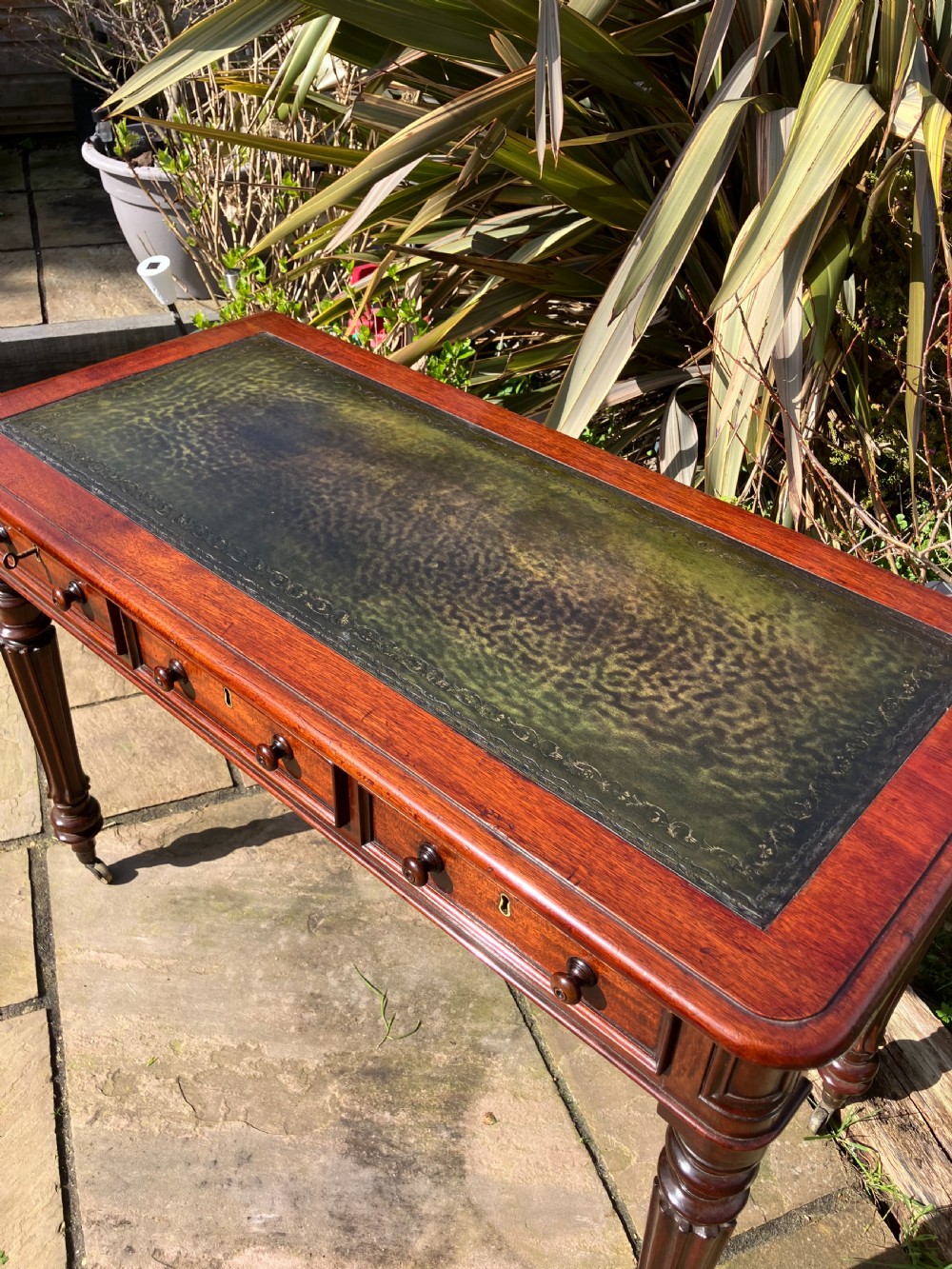 A Victorian mahogany writing table featuring a dark green leather inset top, three frieze drawers with wooden knobs, and turned fluted legs on castors. View III