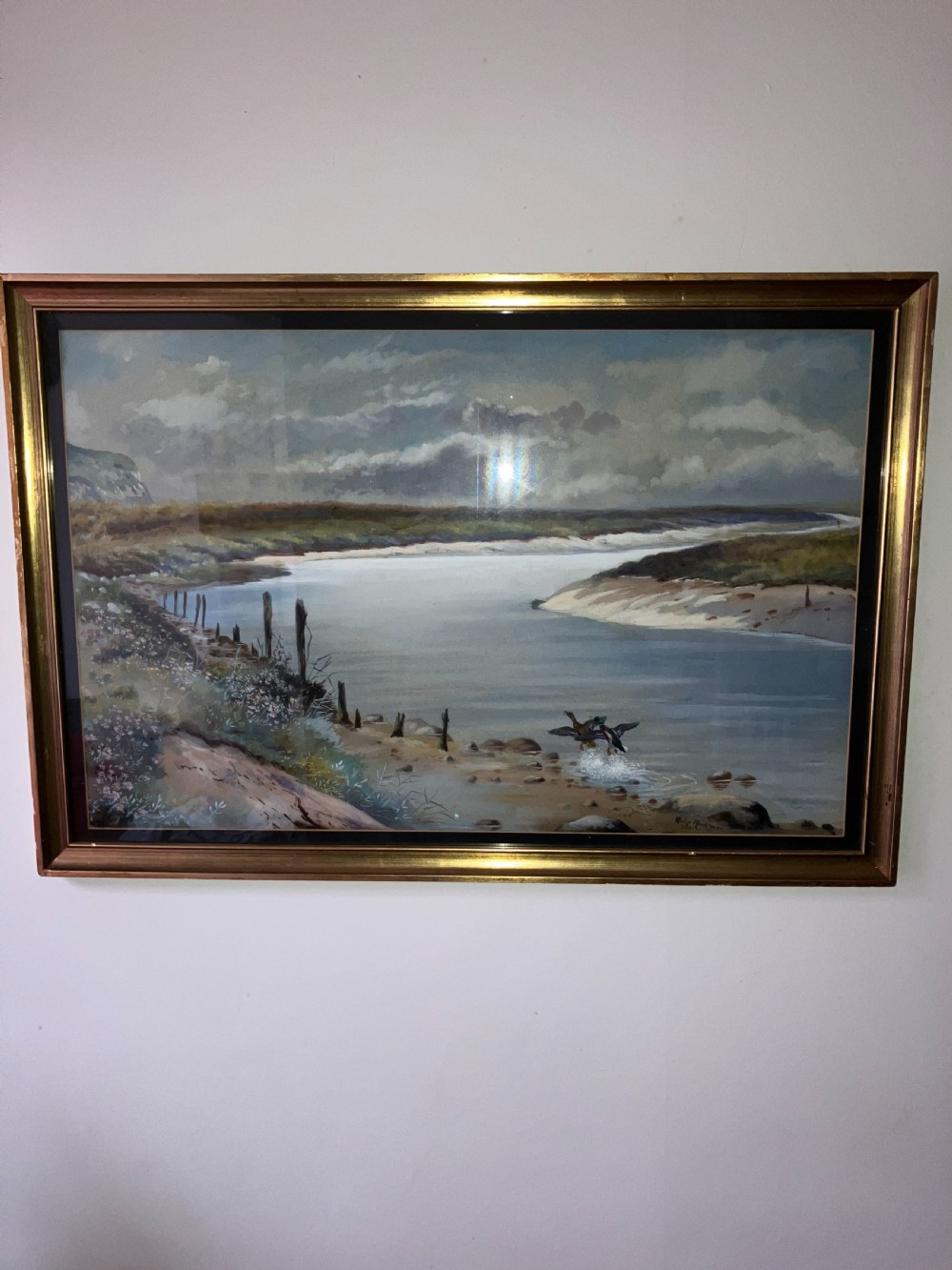 A framed watercolour painting depicting ducks taking flight from a wide river bank under a cloudy sky.