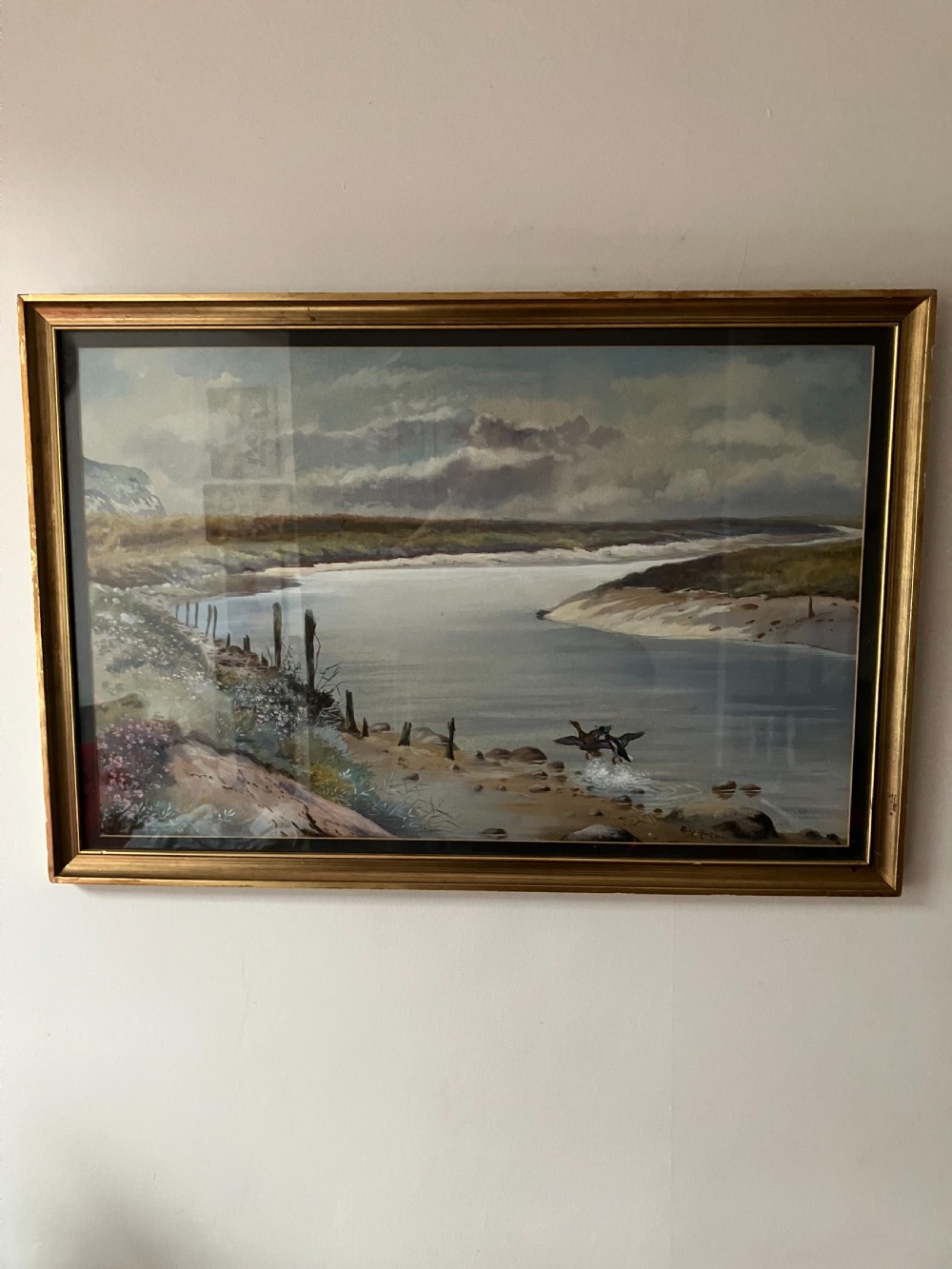 A framed watercolour painting depicting ducks taking flight from a wide river bank under a cloudy sky. View II