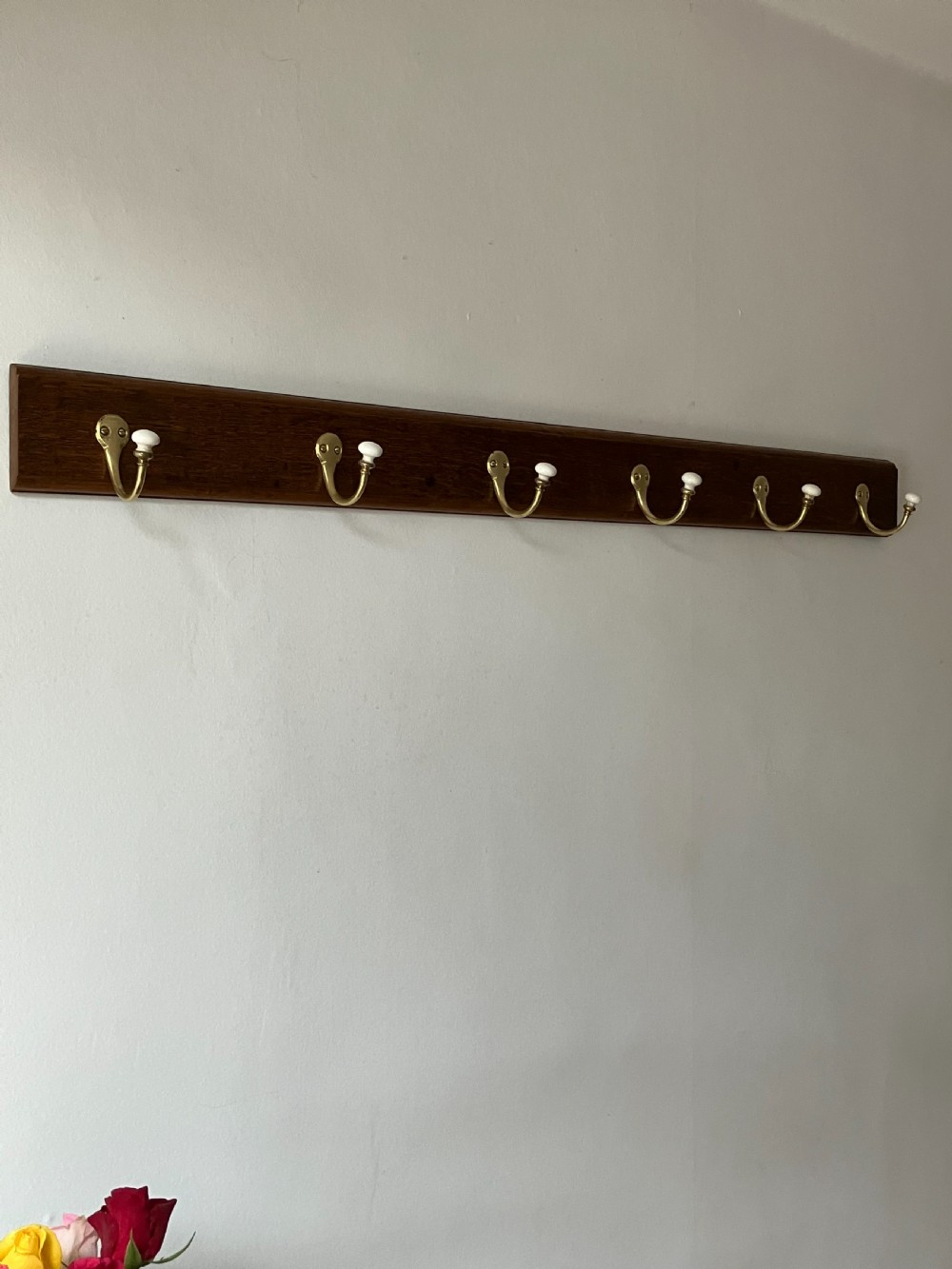 A dark timber wall-mounted rail fitted with six curved brass coat hooks featuring white ceramic knobs.