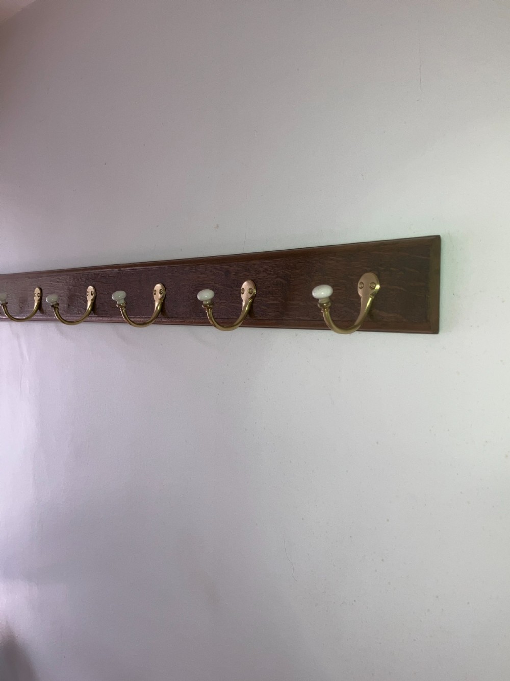 A dark timber wall-mounted rail fitted with six curved brass coat hooks featuring white ceramic knobs. View III
