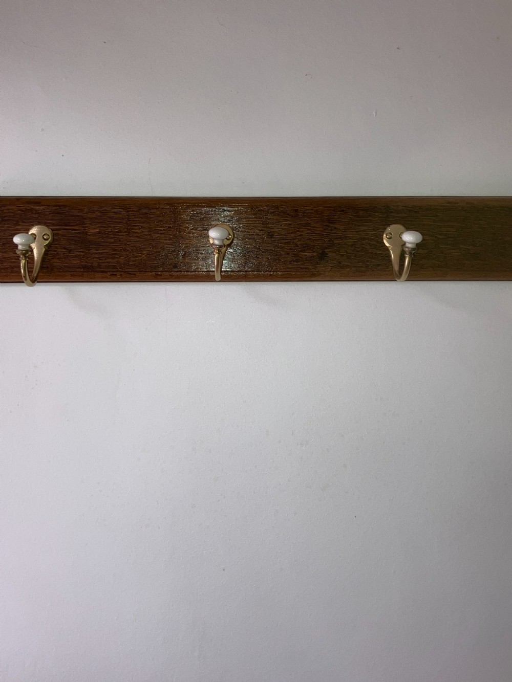 A dark timber wall-mounted rail fitted with six curved brass coat hooks featuring white ceramic knobs. View IV