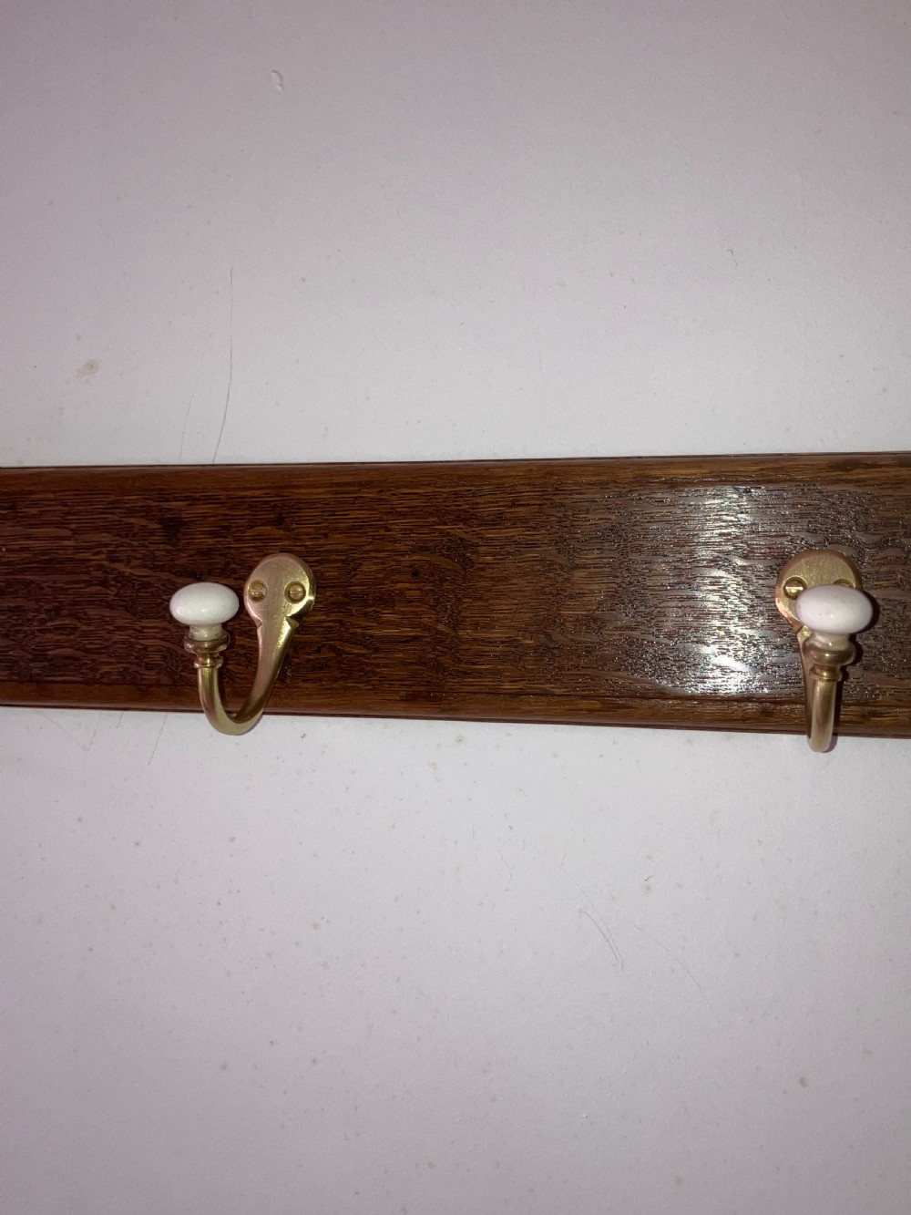 A dark timber wall-mounted rail fitted with six curved brass coat hooks featuring white ceramic knobs. View V