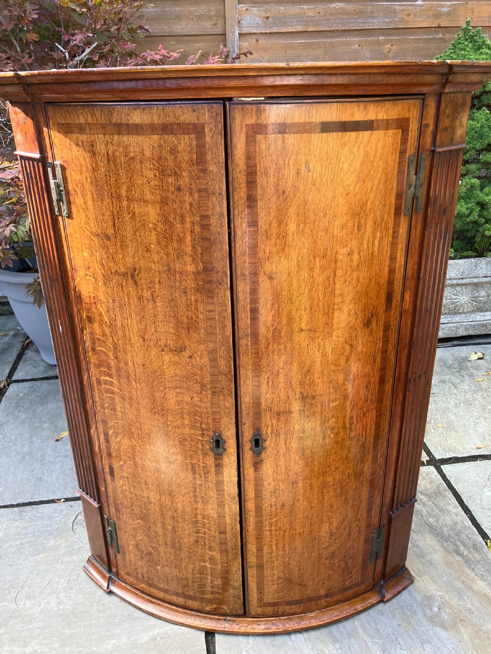A Georgian oak bowfront corner cabinet featuring twin doors with banded inlay, fluted side pilasters, and brass keyhole escutcheons.