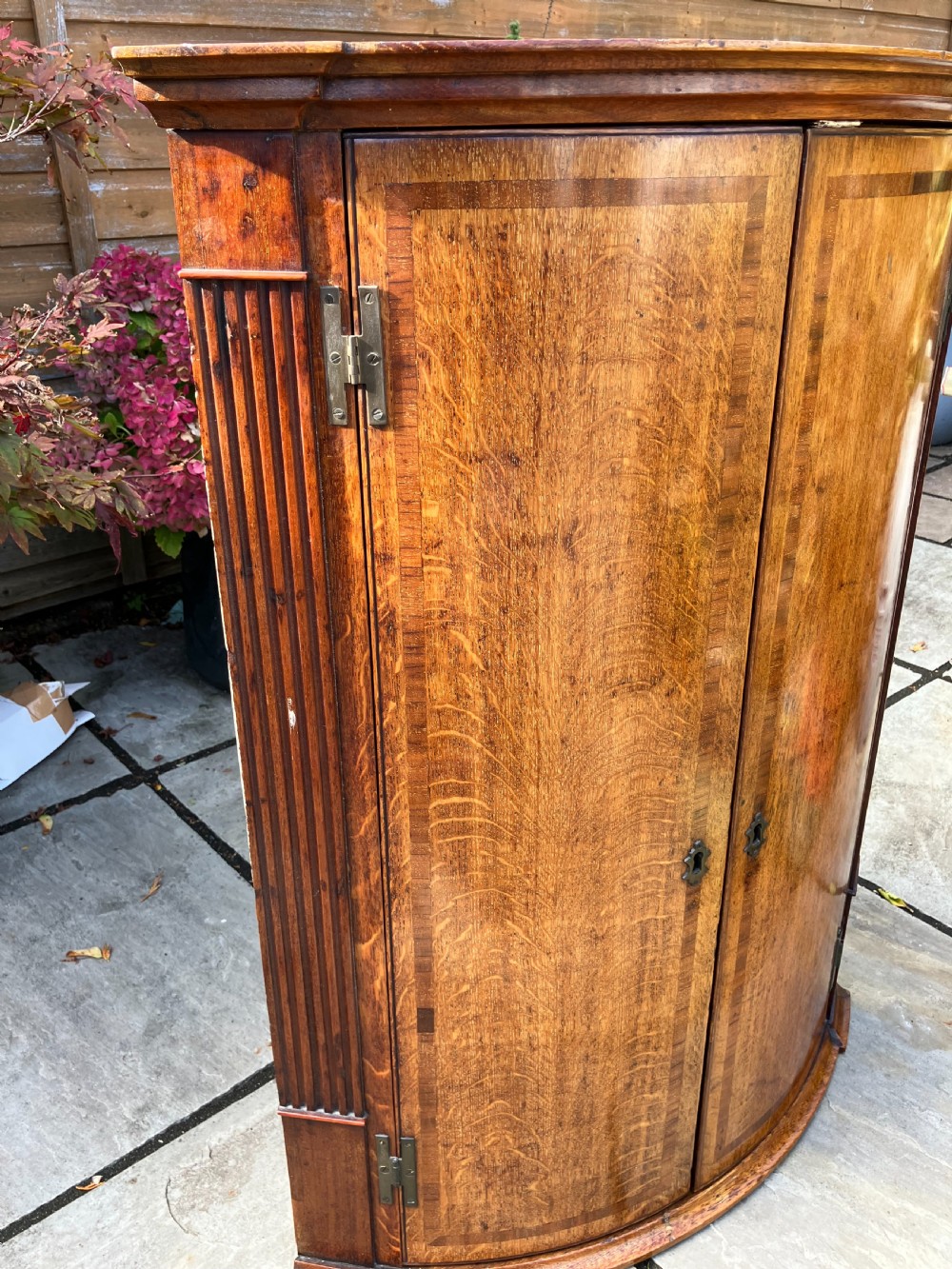 A Georgian oak bowfront corner cabinet featuring twin doors with banded inlay, fluted side pilasters, and brass keyhole escutcheons. View II
