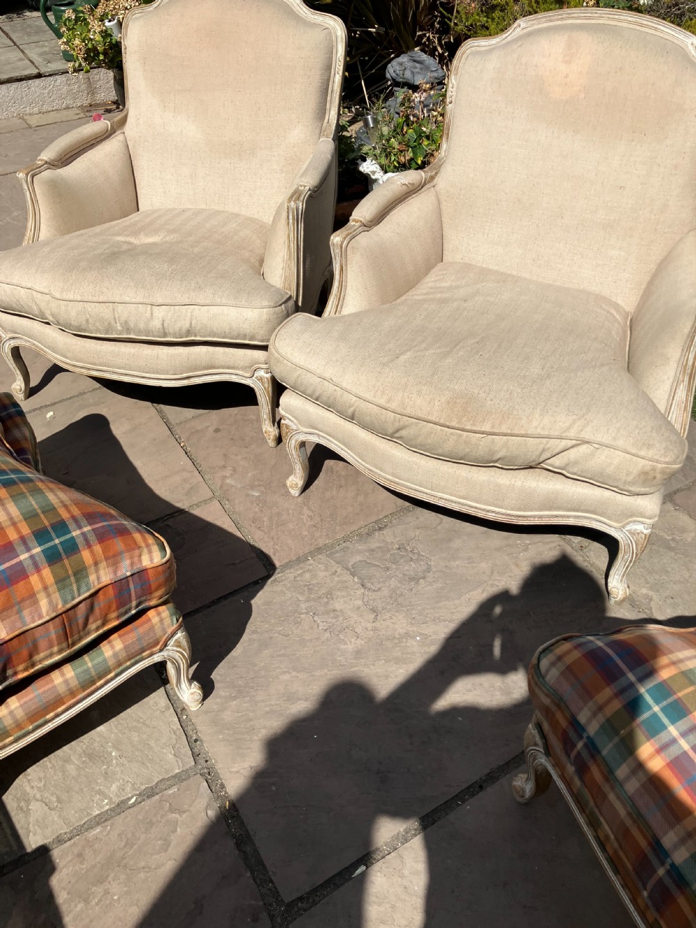 A pair of French Louis XV style bergere armchairs featuring neutral fabric upholstery, distressed white painted timber frames, and carved cabriole legs.