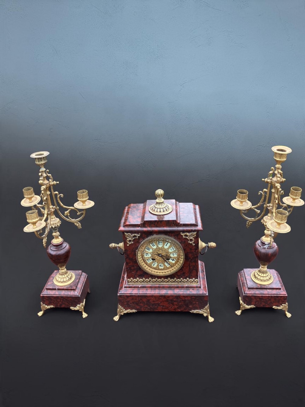 A three-piece French garniture set comprising a central rouge marble mantel clock with gilt brass mounts flanked by two matching multi-branch candelabras.