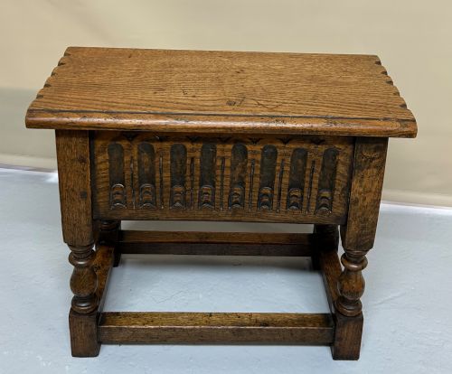 fig 1. A solid oak Jacobean style box stool featuring a carved decorative apron, turned legs, lower stretchers, and a flat hinged top.