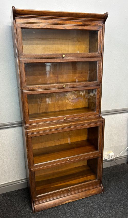 fig 1. A five-tier oak barrister bookcase with glazed up-and-over doors and small brass knobs.