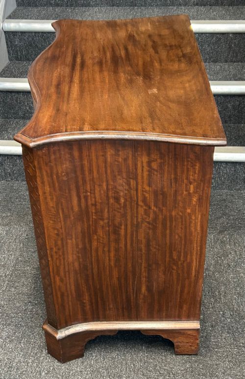 fig 1. A Georgian Revival mahogany chest of drawers featuring a serpentine front, four graduated drawers with brass handles, blind fretwork on canted corners, and bracket feet.