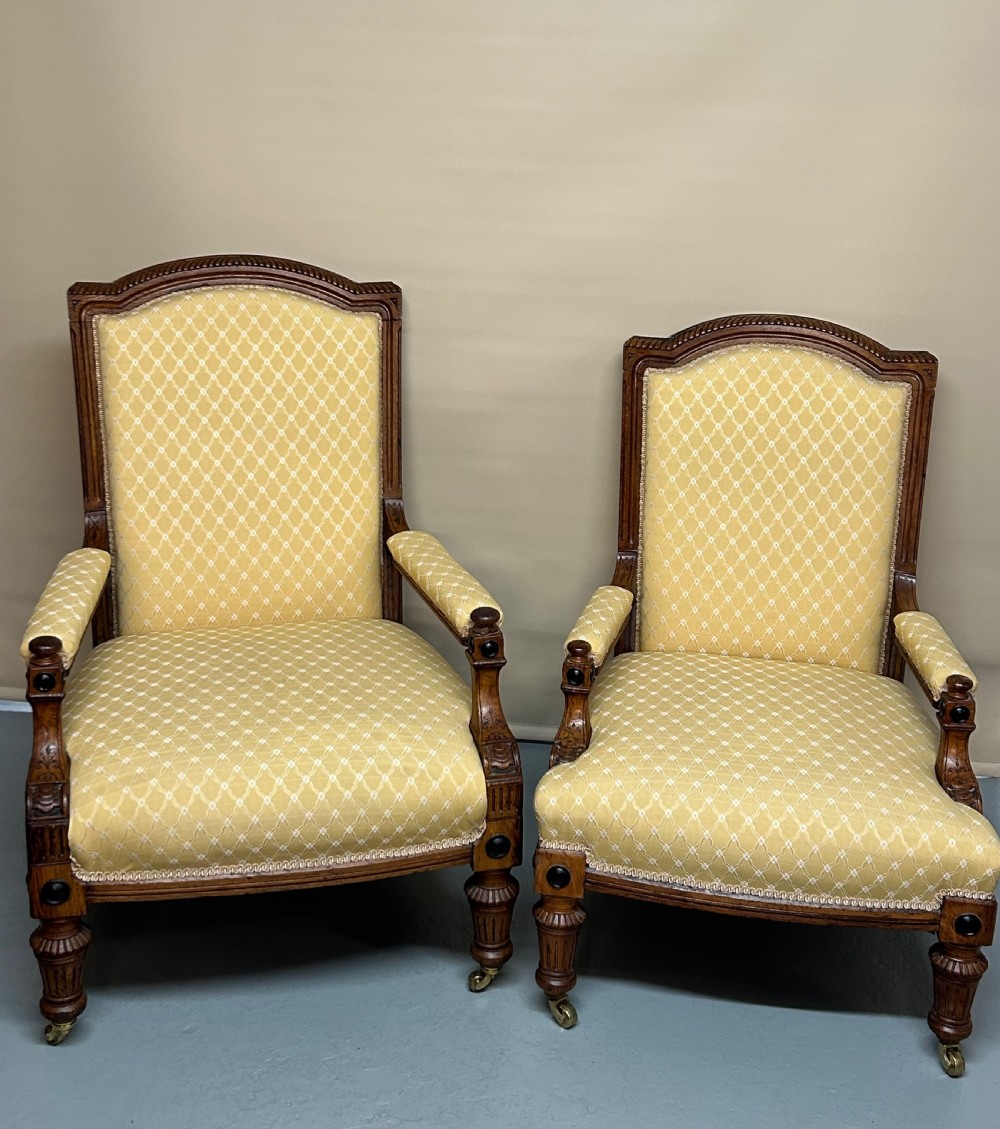 A pair of Victorian pollard oak armchairs upholstered in yellow patterned fabric featuring reeded turned legs and brass castors.