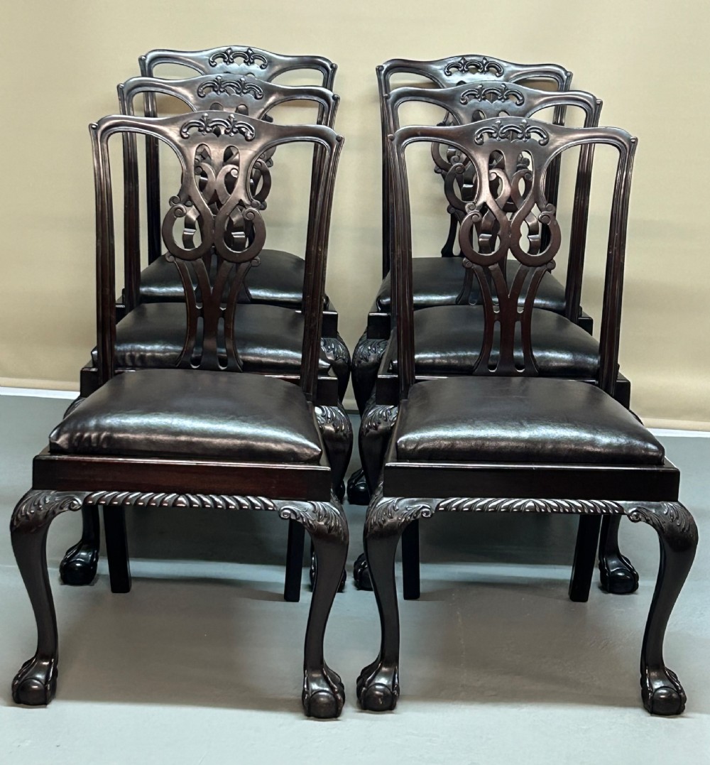A set of six dark mahogany Chippendale style dining chairs featuring carved pierced back splats, dark leather seats, and front cabriole legs with ball and claw feet.