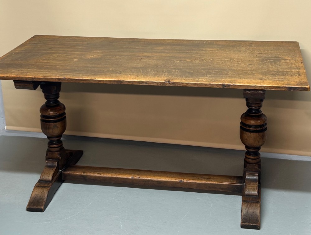 A solid oak refectory dining table featuring a rectangular top, heavy turned baluster legs, and a low central stretcher.