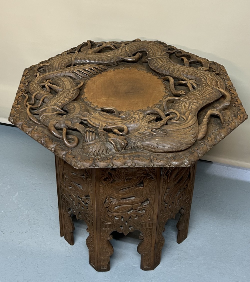 An octagonal wooden side table with high-relief carvings of dragons across the top surface and pierced base.