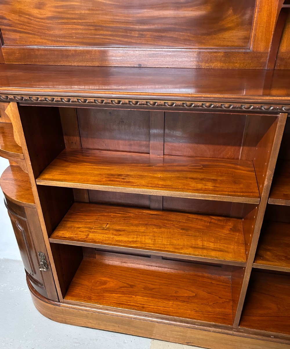 A large Victorian mahogany corner bookcase featuring open shelves along one section, a central panelled door cupboard, and an elevated glazed corner cabinet topped with a swan-neck pediment. View XIII