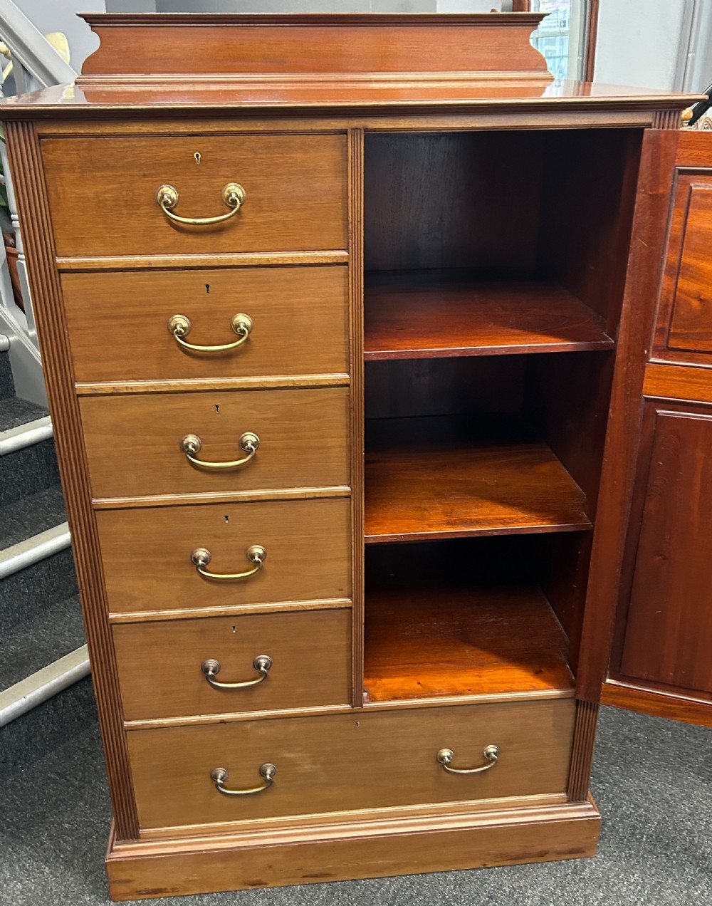 A tall mahogany gentlemans chest featuring five left-hand drawers beside a panelled cupboard door, over a wide base drawer with brass handles. View VI
