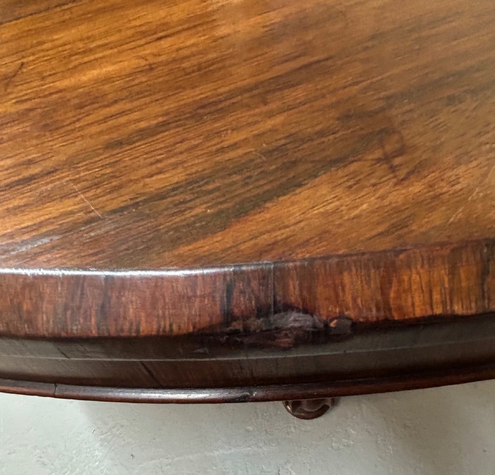 A circular William IV tilt-top rosewood breakfast table featuring dark figured grain, shown upright on a circular plinth base with carved scroll feet. View VI