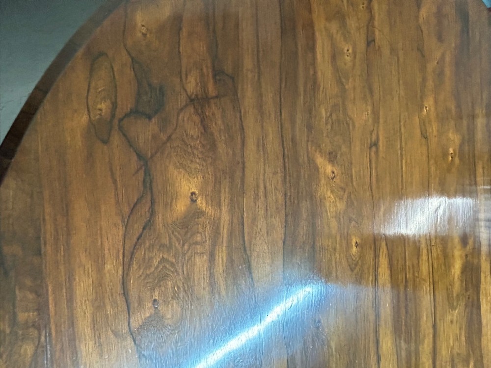 A circular William IV tilt-top rosewood breakfast table featuring dark figured grain, shown upright on a circular plinth base with carved scroll feet. View VII