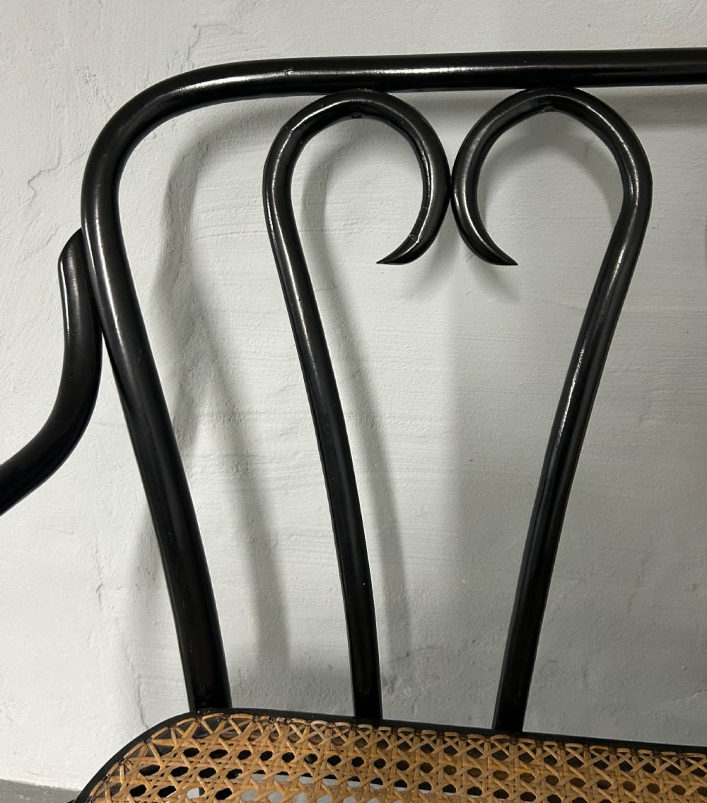 A black painted bentwood two-seater bench featuring three heart-shaped backrest scrolls and a woven natural rattan cane seat. View III