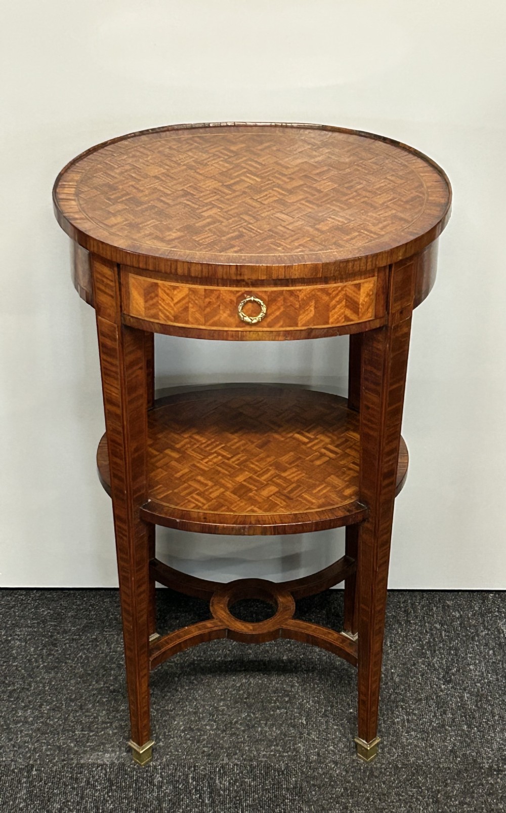 A French-style kingswood side table featuring a geometric parquetry top, a small drawer with a brass ring pull, a lower undershelf, and curved cross-stretchers.