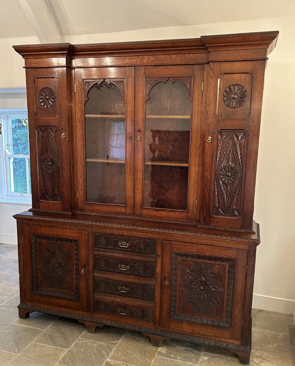 Large carved dark oak bookcase featuring glazed central doors and carved side panels above a base cupboard with drawers.