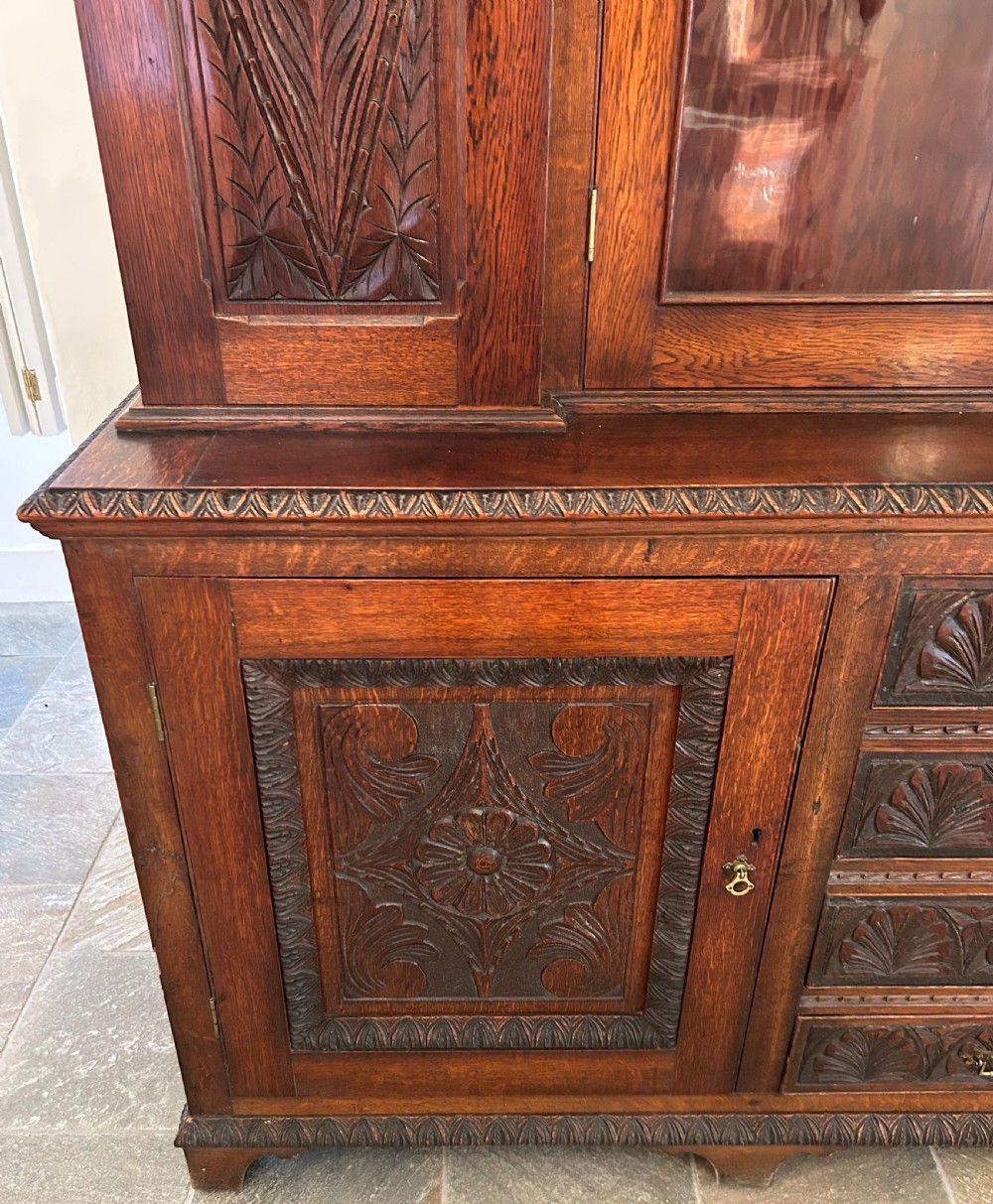 Large carved dark oak bookcase featuring glazed central doors and carved side panels above a base cupboard with drawers. View V