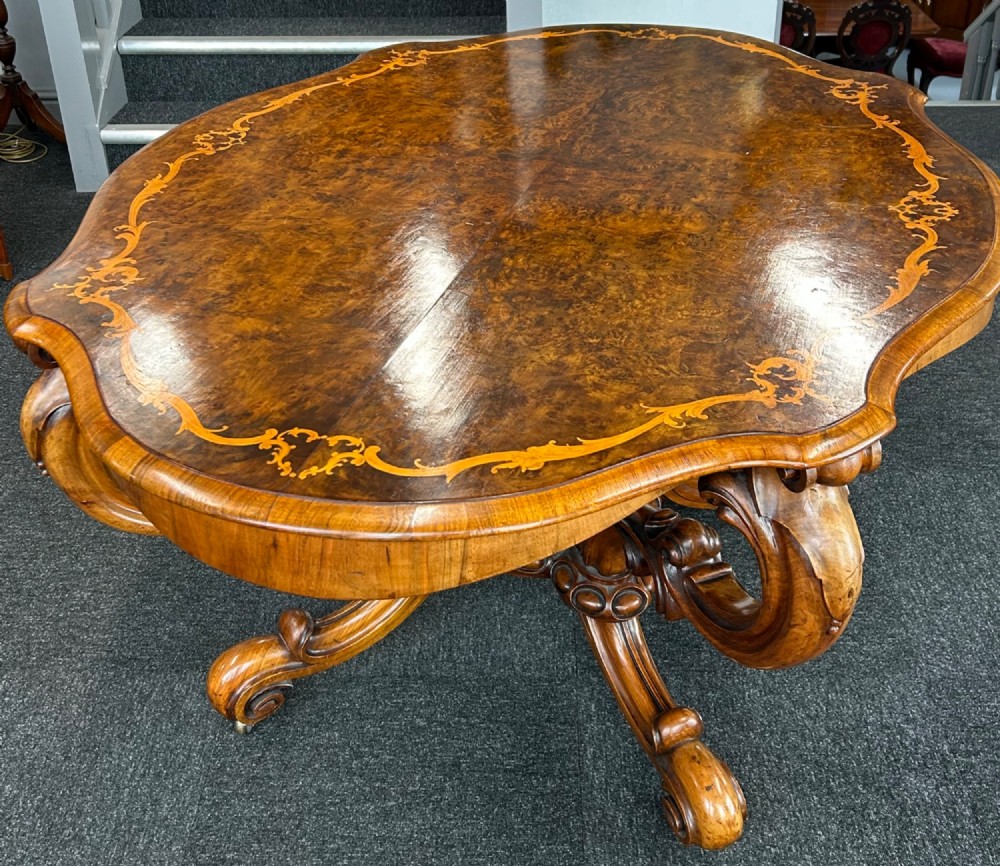 A Victorian burr walnut centre table featuring a serpentine shaped top with marquetry inlay and carved cabriole legs.