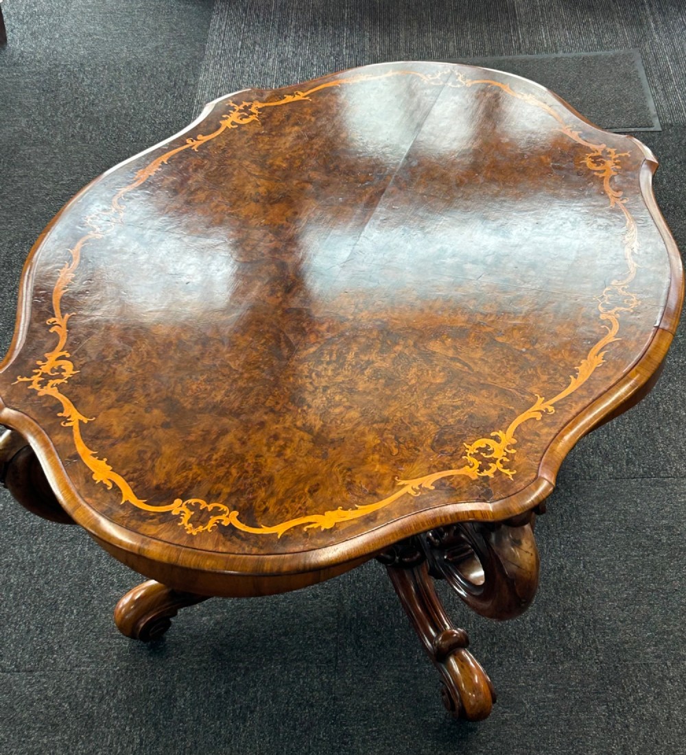 A Victorian burr walnut centre table featuring a serpentine shaped top with marquetry inlay and carved cabriole legs. View II