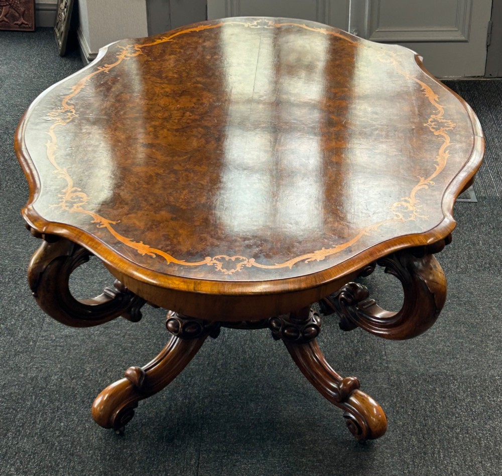 A Victorian burr walnut centre table featuring a serpentine shaped top with marquetry inlay and carved cabriole legs. View III