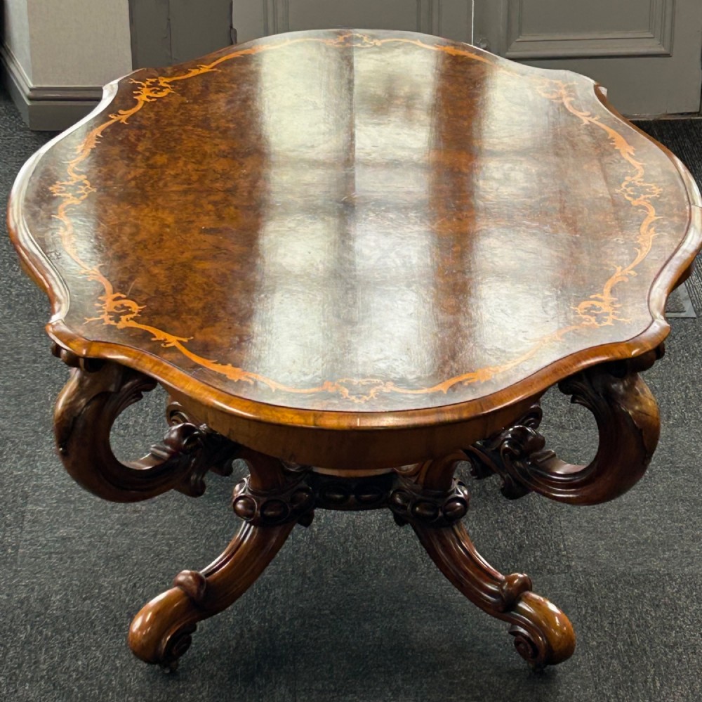A Victorian burr walnut centre table featuring a serpentine shaped top with marquetry inlay and carved cabriole legs. View IV