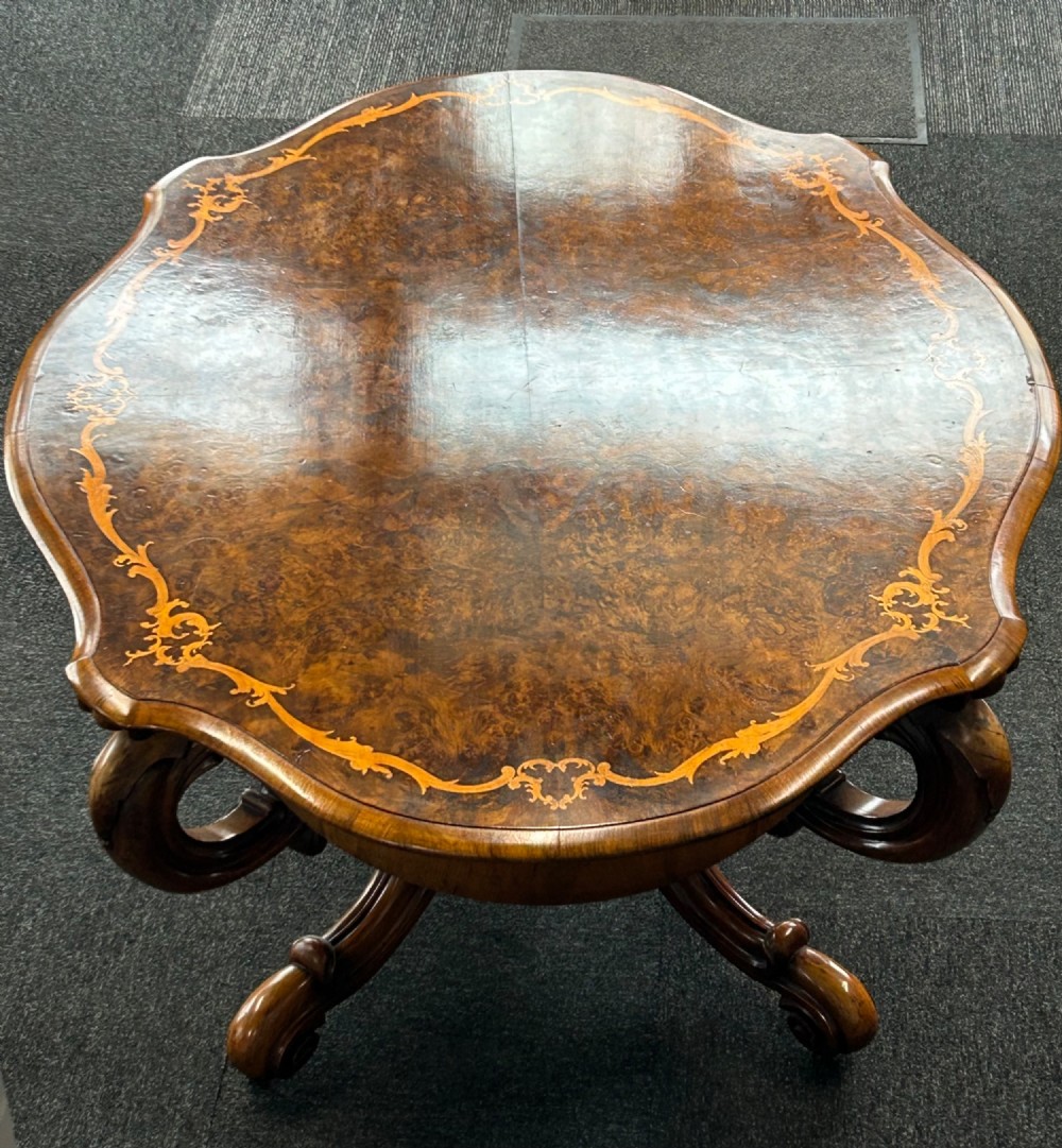 A Victorian burr walnut centre table featuring a serpentine shaped top with marquetry inlay and carved cabriole legs. View VII