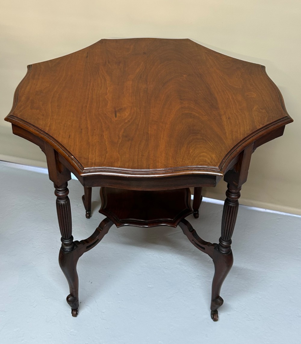 An Edwardian walnut occasional table with a shaped octagonal top, lower tier shelf, turned legs, and small castors.