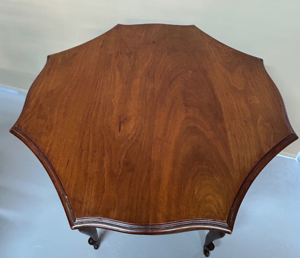 An Edwardian walnut occasional table with a shaped octagonal top, lower tier shelf, turned legs, and small castors. View II