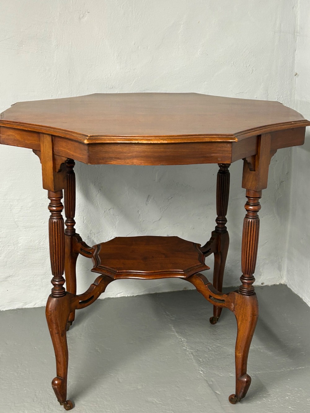An Edwardian walnut occasional table with a shaped octagonal top, lower tier shelf, turned legs, and small castors. View IV