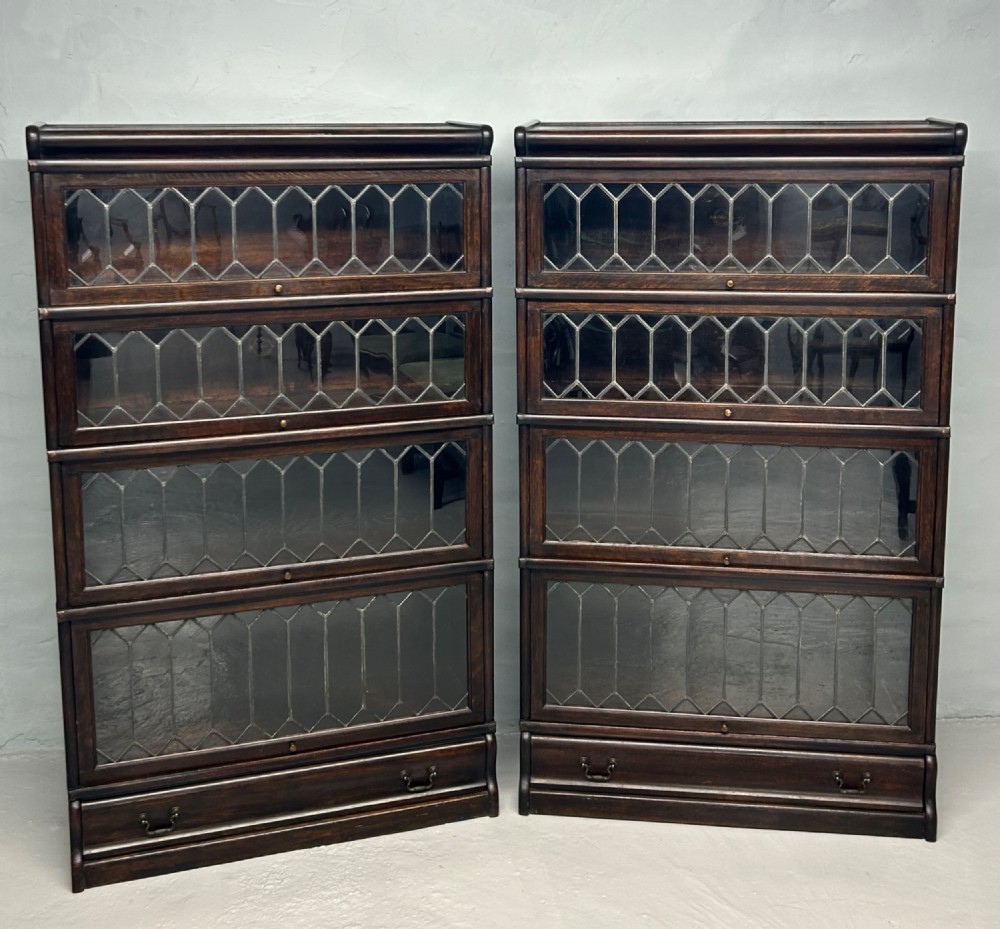 A pair of dark oak Globe Wernicke sectional bookcases featuring four leaded glass door compartments and a base drawer each.