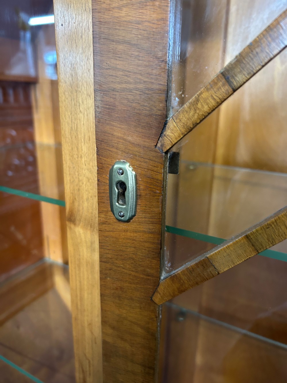 An octagonal Art Deco walnut display cabinet featuring a central glazed door with diagonal glazing bars and glass interior shelves on a flared plinth base. View VII
