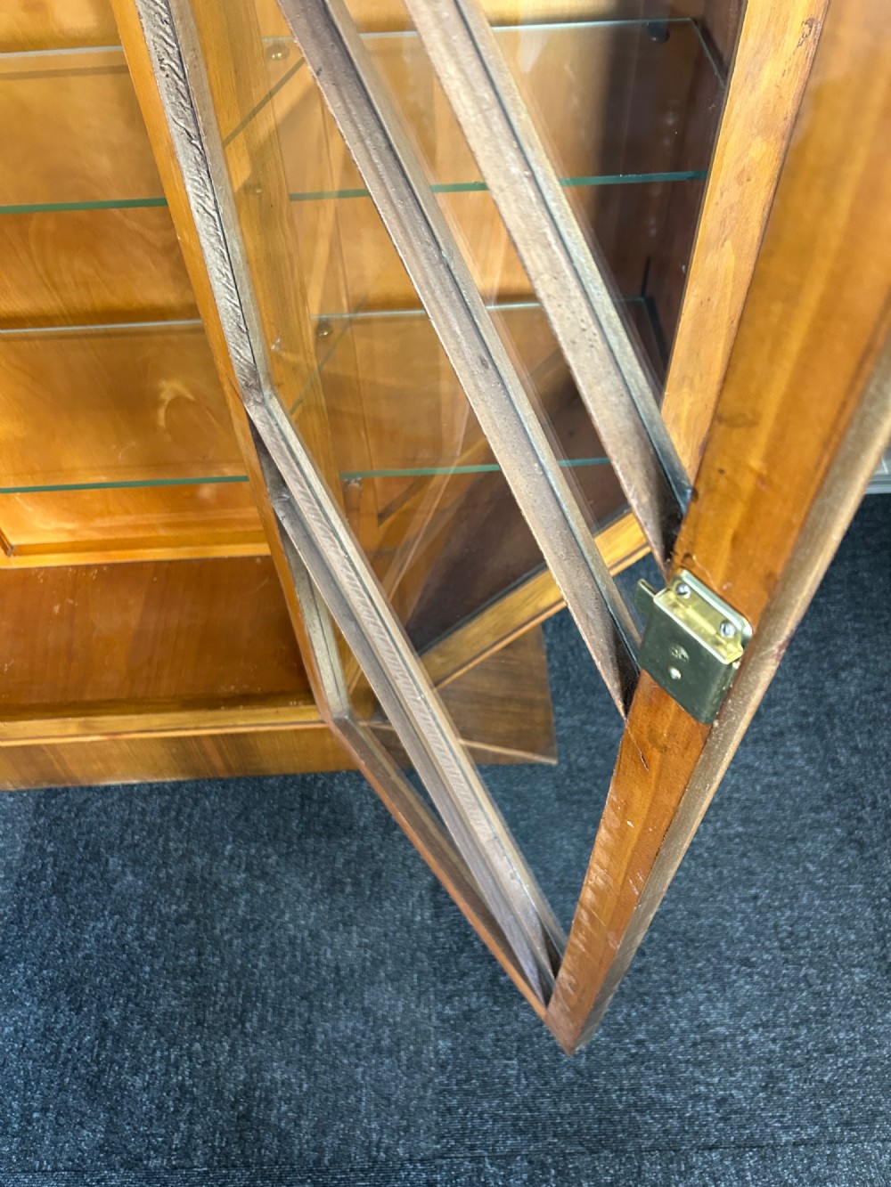 An octagonal Art Deco walnut display cabinet featuring a central glazed door with diagonal glazing bars and glass interior shelves on a flared plinth base. View VIII