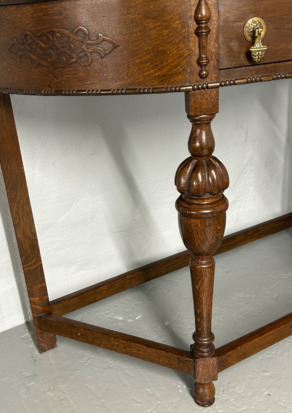 A 1920s dark oak demi-lune console table featuring a carved strapwork drawer, turned front legs, and a low gallery back. View III