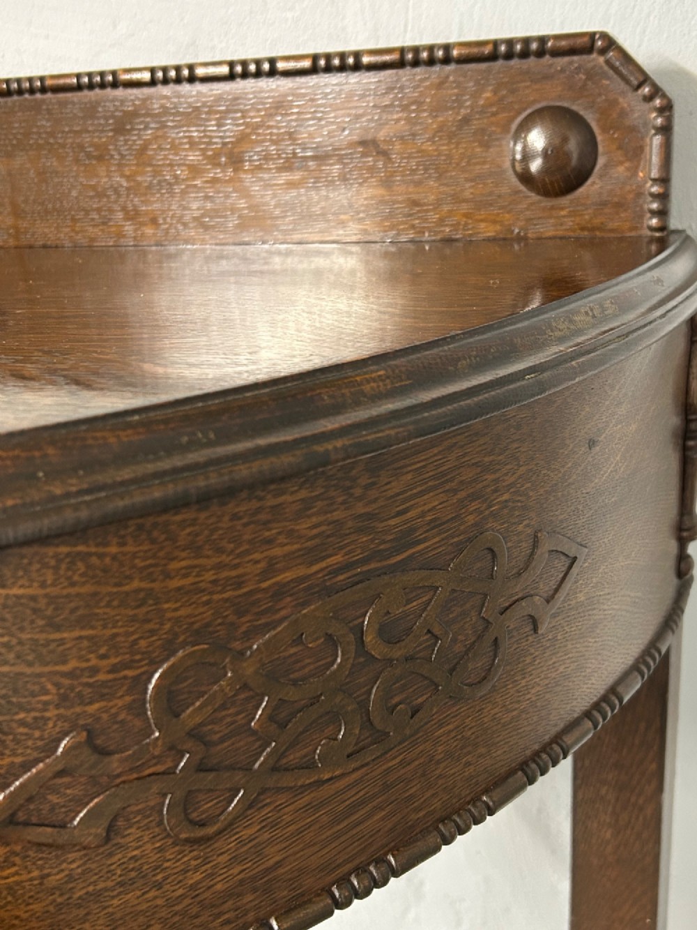 A 1920s dark oak demi-lune console table featuring a carved strapwork drawer, turned front legs, and a low gallery back. View IV
