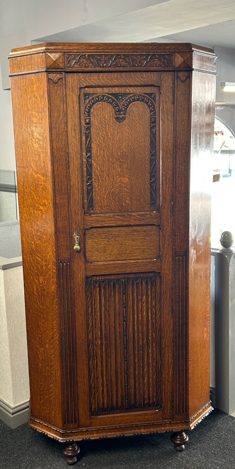 A tall 1920s solid oak hall robe featuring a single door with carved arcading and linenfold panelling, canted sides, and turned feet.