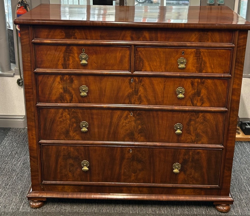 A nineteenth-century Victorian flame mahogany chest of drawers featuring two short drawers over three long graduated drawers with decorative brass drop handles and bun feet.