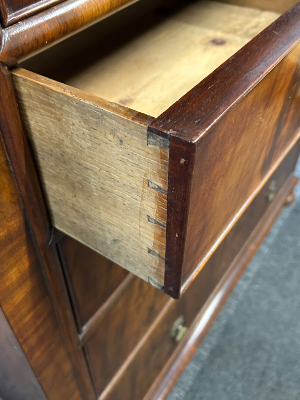 A nineteenth-century Victorian flame mahogany chest of drawers featuring two short drawers over three long graduated drawers with decorative brass drop handles and bun feet. View IV