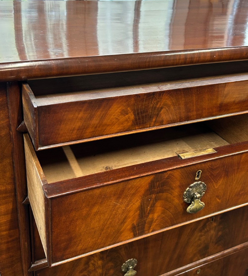 A nineteenth-century Victorian flame mahogany chest of drawers featuring two short drawers over three long graduated drawers with decorative brass drop handles and bun feet. View V