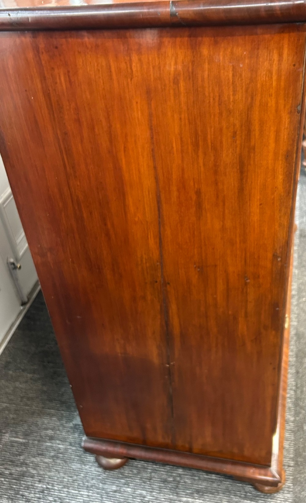 A nineteenth-century Victorian flame mahogany chest of drawers featuring two short drawers over three long graduated drawers with decorative brass drop handles and bun feet. View VII
