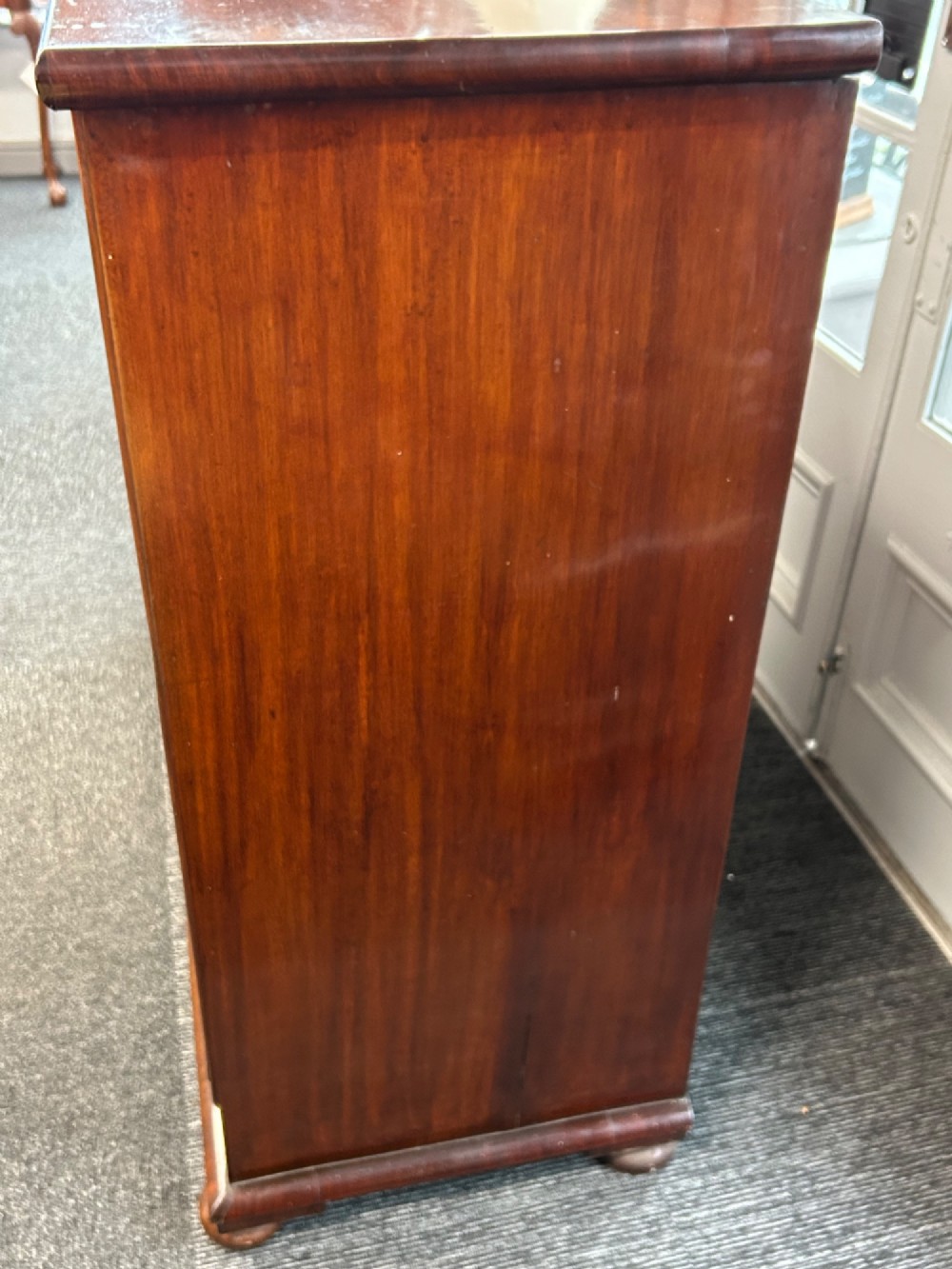 A nineteenth-century Victorian flame mahogany chest of drawers featuring two short drawers over three long graduated drawers with decorative brass drop handles and bun feet. View VIII