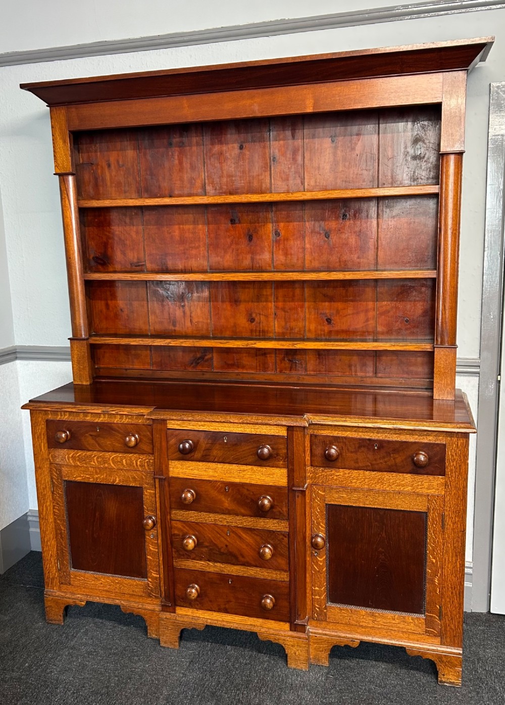 An antique oak Welsh dresser featuring an upper open plate rack with shelves and a lower breakfront base with central drawers flanked by cupboards.