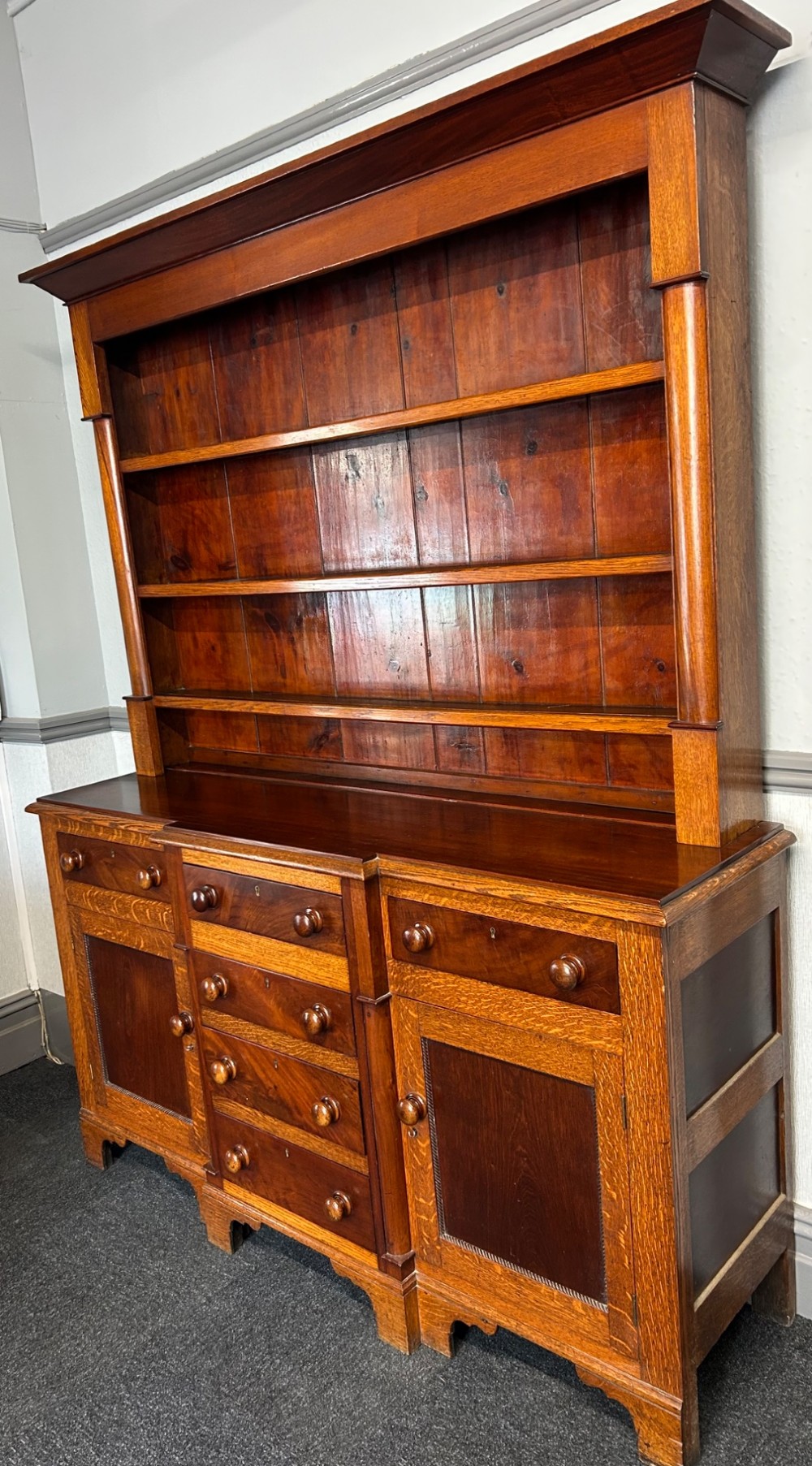 An antique oak Welsh dresser featuring an upper open plate rack with shelves and a lower breakfront base with central drawers flanked by cupboards. View II
