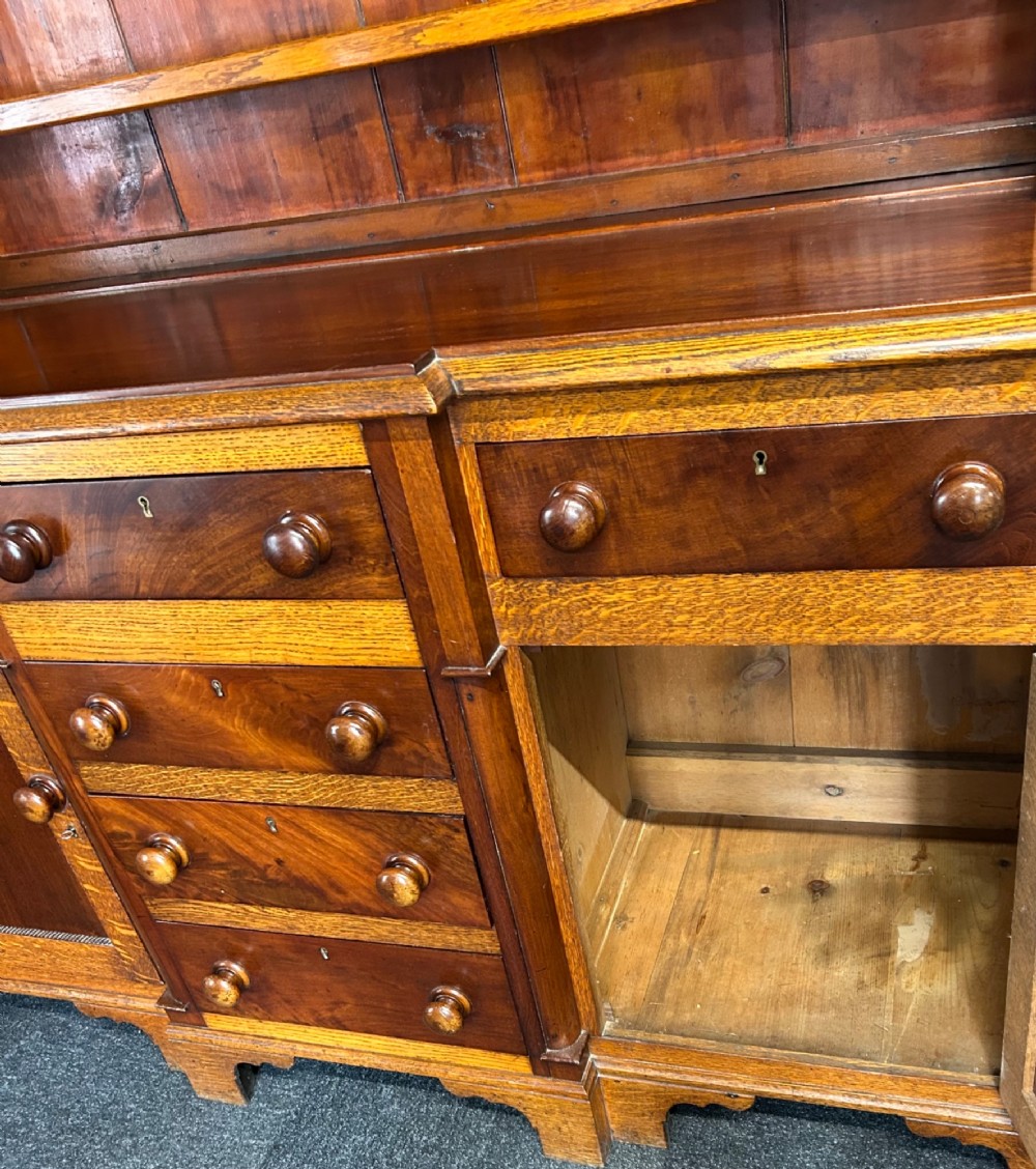An antique oak Welsh dresser featuring an upper open plate rack with shelves and a lower breakfront base with central drawers flanked by cupboards. View VI