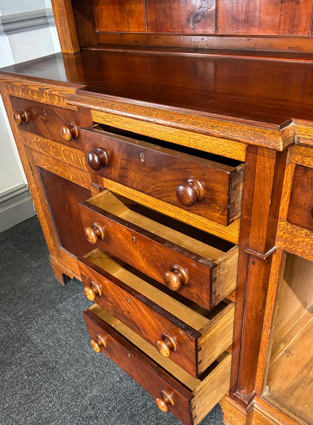 An antique oak Welsh dresser featuring an upper open plate rack with shelves and a lower breakfront base with central drawers flanked by cupboards. View VII